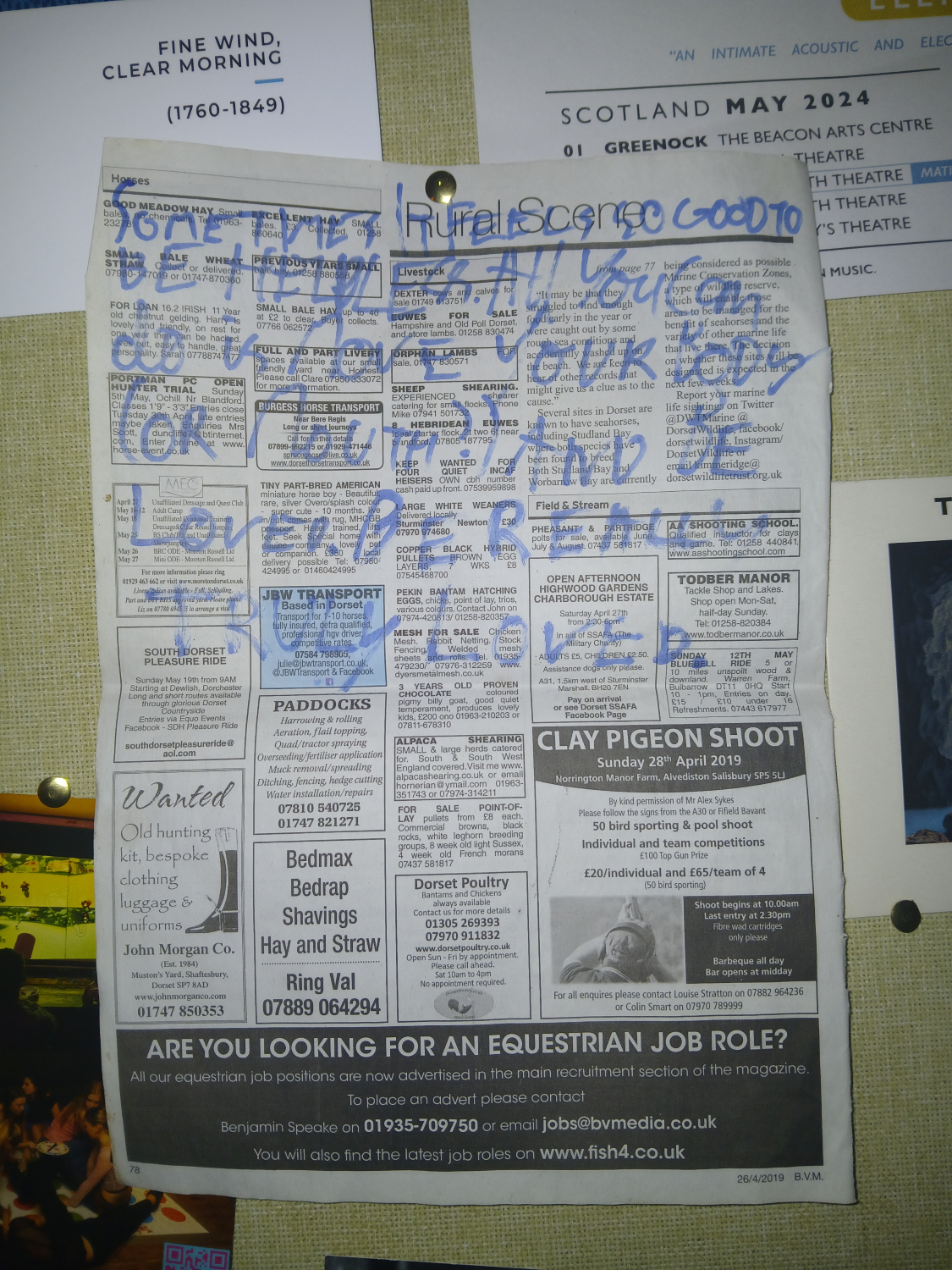 The original. The words above, scrawled in thick blue pen on a sheet of newspaper. The paper is pinned to a pinboard with various corners of posters and pieces of paper around it